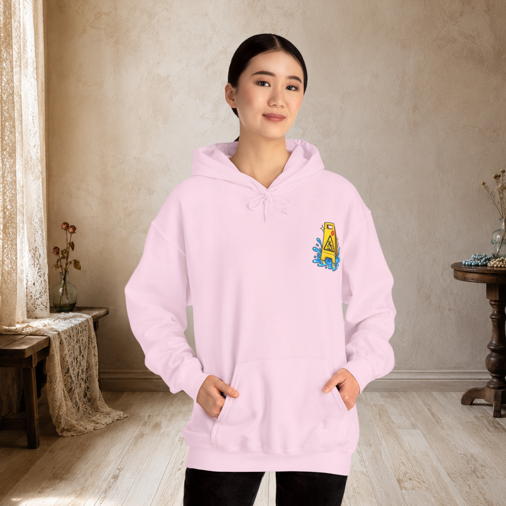Female model wearing a light pink unisex hoodie showing the small wet-floor caution graphic on the front