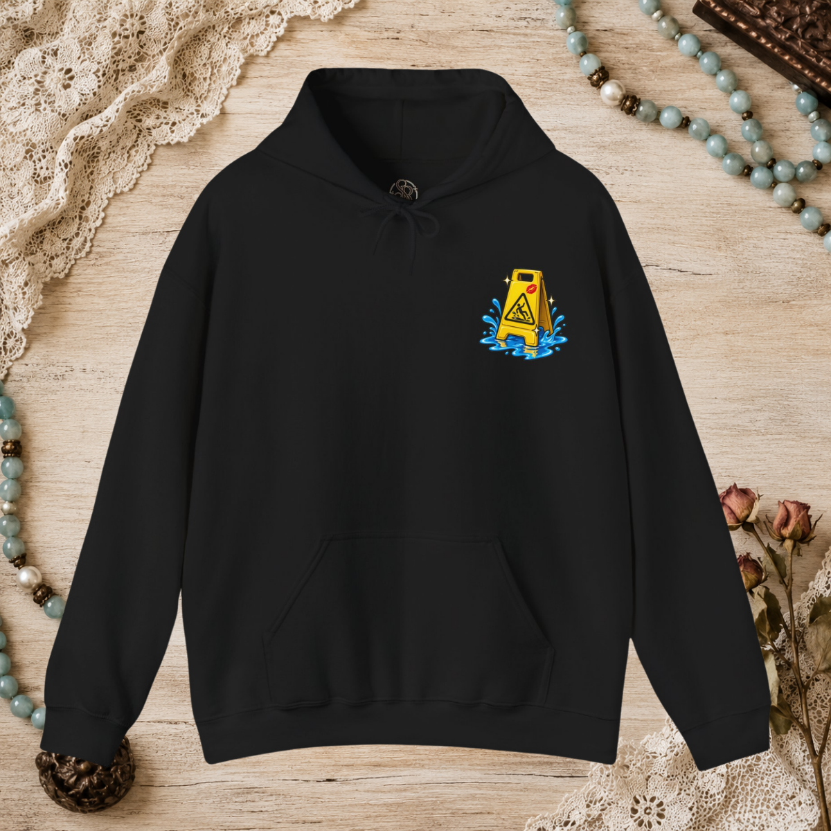 Front of a black unisex hoodie with a small yellow wet-floor caution graphic on the left chest
