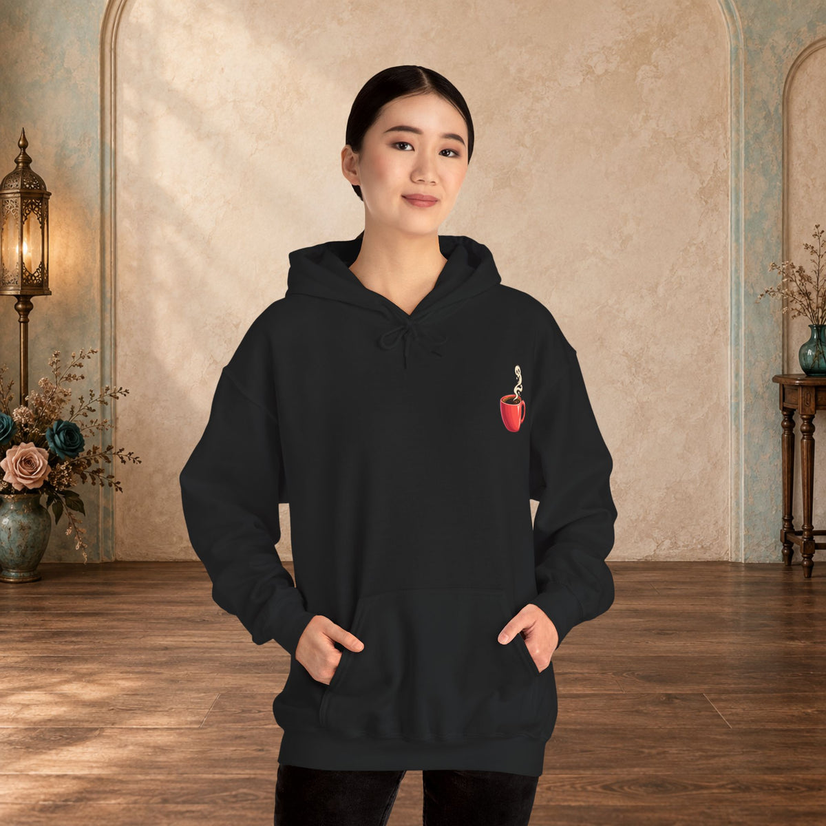 Female model wearing a black hoodie with a small red coffee cup and heart-steam design on the front