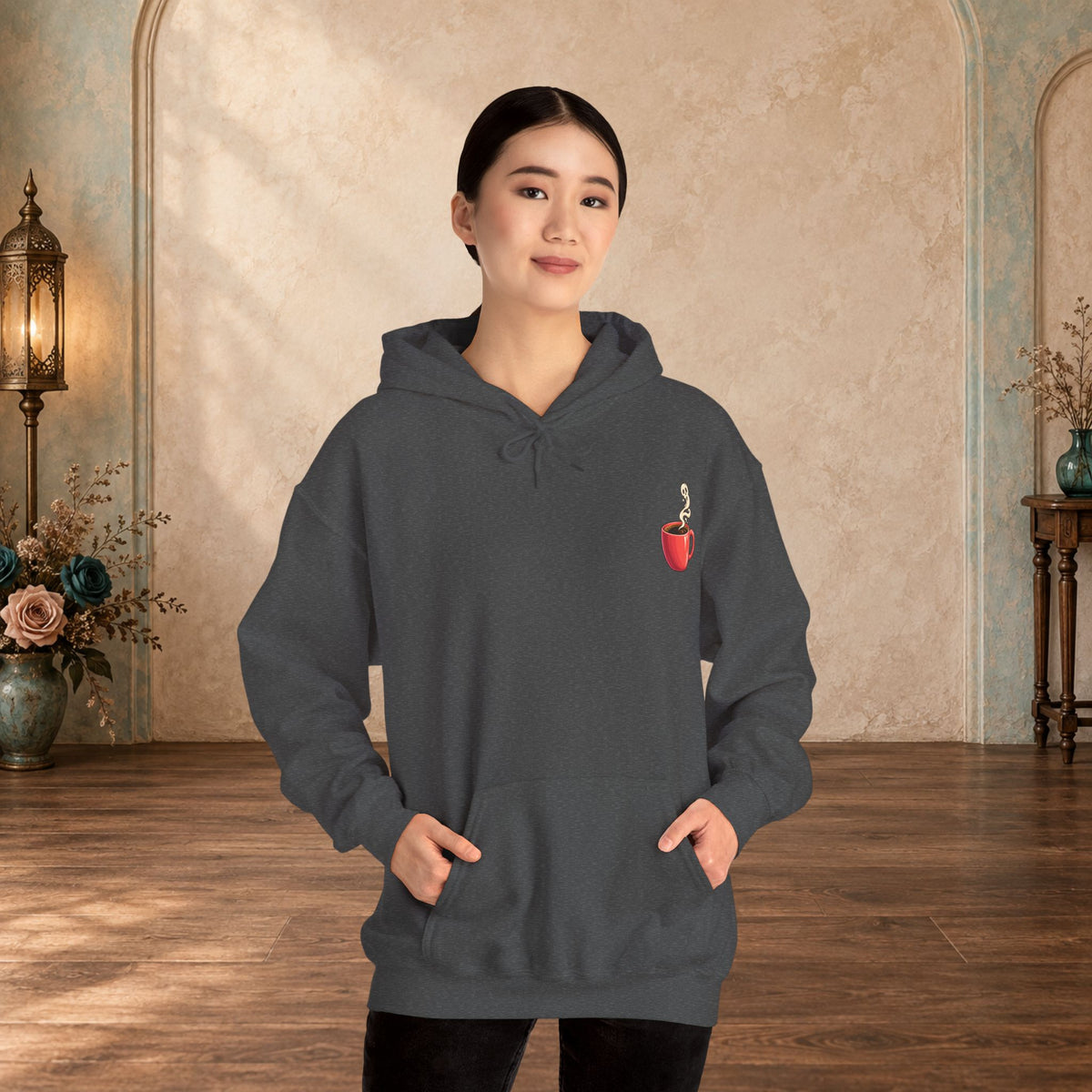 Female model wearing a Dark Heather hoodie with a small red coffee cup and heart-steam design on the front