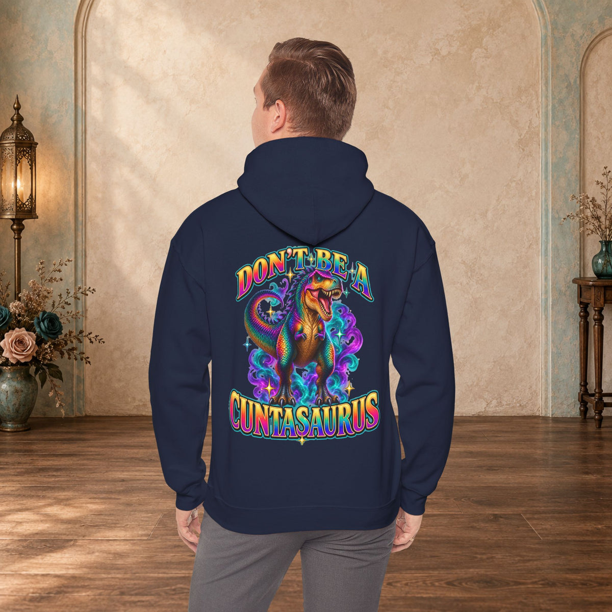 Man wearing a navy Don’t Be a Cuntasaurus hoodie with a colorful T. rex back print