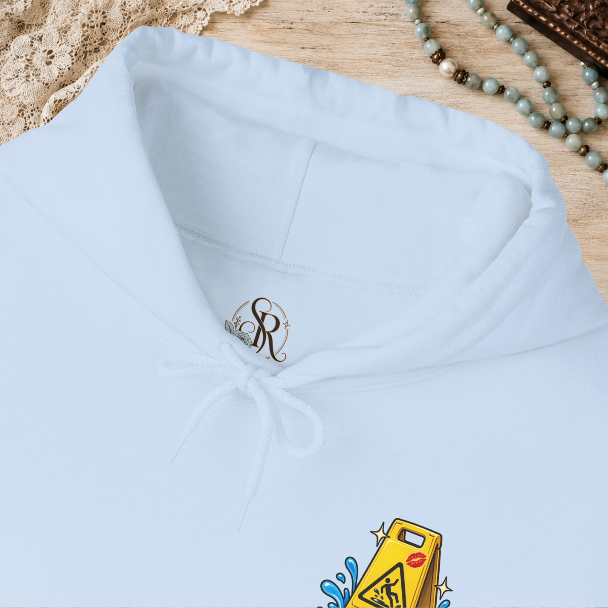 Scorpion Rose Designs custom hoodie neck label with size, fiber content, country of origin, and care symbols on light blue hoodie